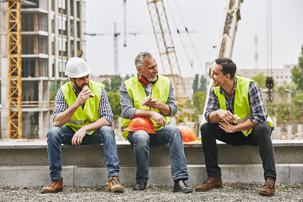 Three construction workers taking a break and eating their lunch on a job site.