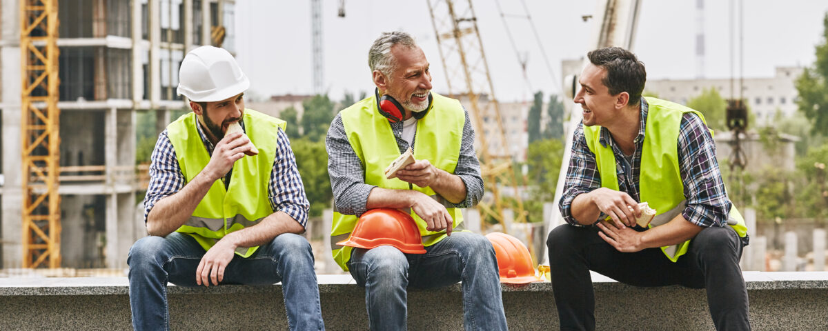 Three construction workers taking a break and eating their lunch on a job site.