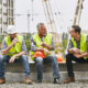 Three construction workers taking a break and eating their lunch on a job site.