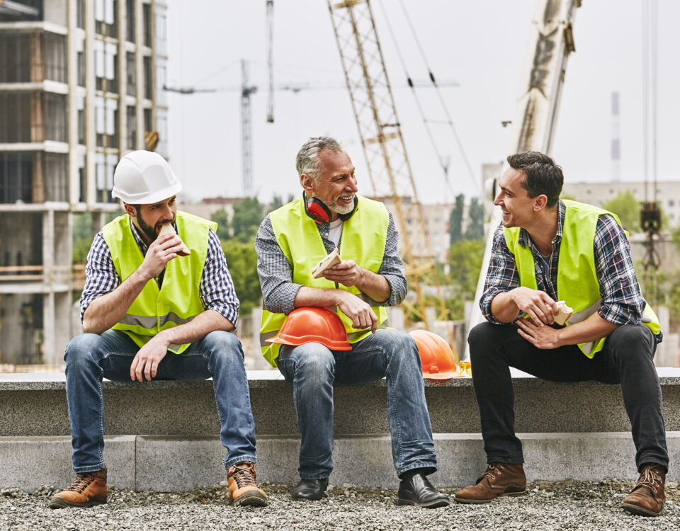 Three construction workers taking a break and eating their lunch on a job site.