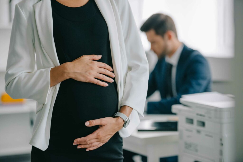 Pregnant woman holding her belly while at work with a colleague in the background