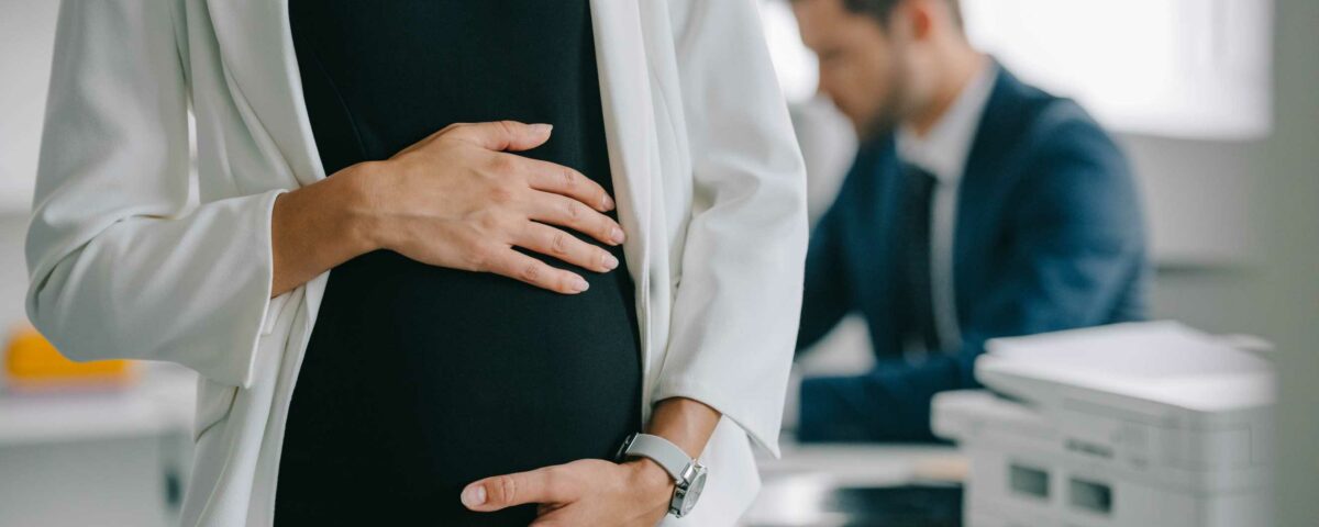 Pregnant woman holding her belly while at work with a colleague in the background