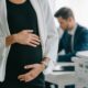 Pregnant woman holding her belly while at work with a colleague in the background