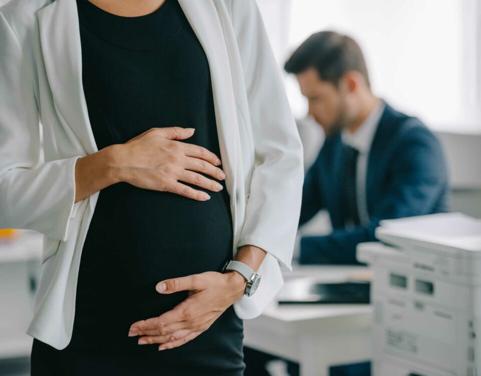 Pregnant woman holding her belly while at work with a colleague in the background