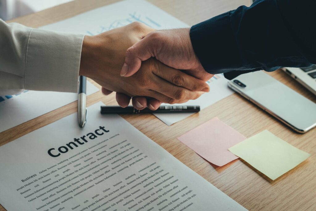 Two people shaking hands over a contract